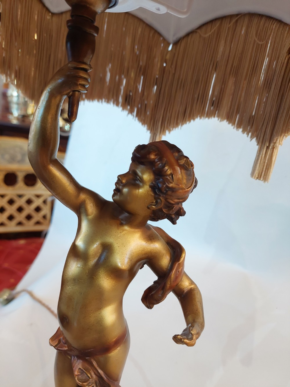 A cast bronze cherub statuette holding aloft a dome-shaped lampshade with patterned fabric and beaded tassel fringe, set on a dark marble base. View III