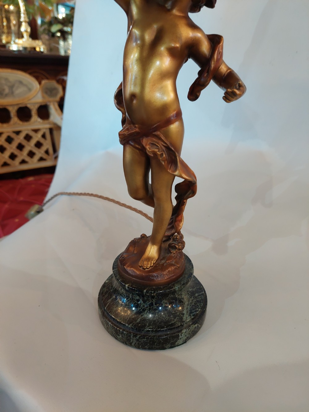 A cast bronze cherub statuette holding aloft a dome-shaped lampshade with patterned fabric and beaded tassel fringe, set on a dark marble base. View V