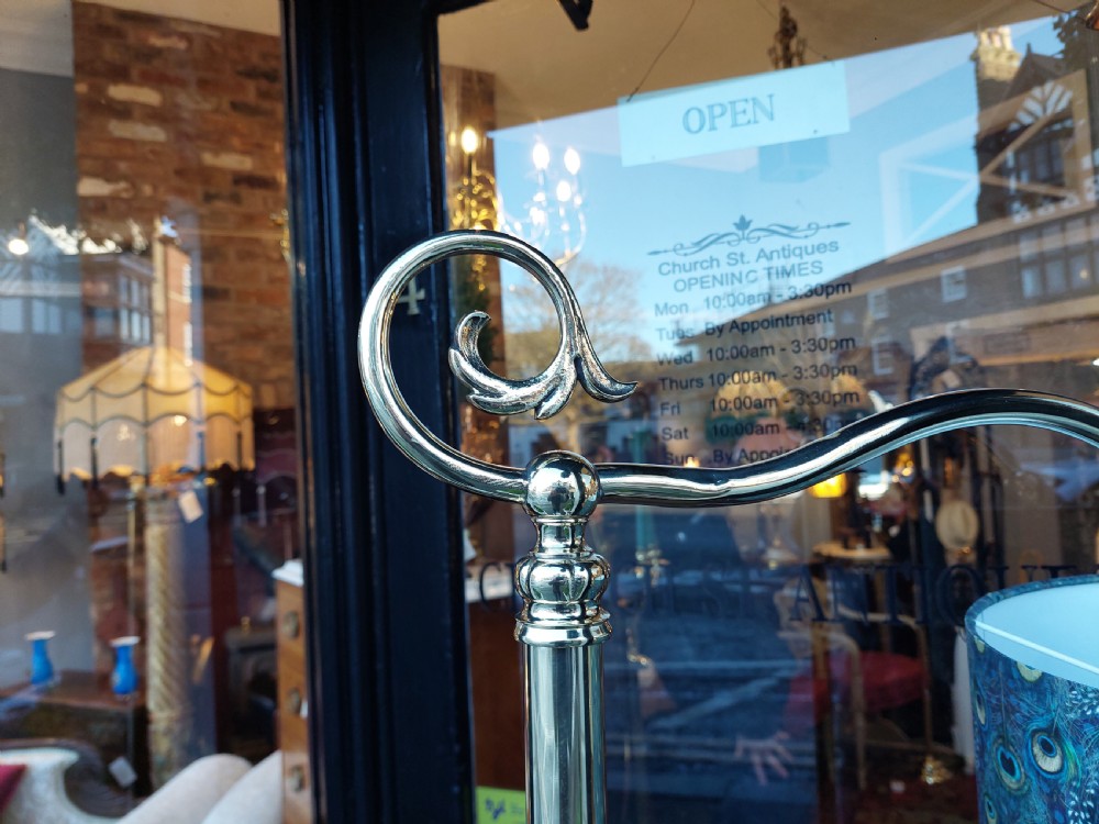 A tall silver-coloured metal standard lamp featuring a scrolled top arm, tripodal base, and a blue patterned fabric shade. View VI