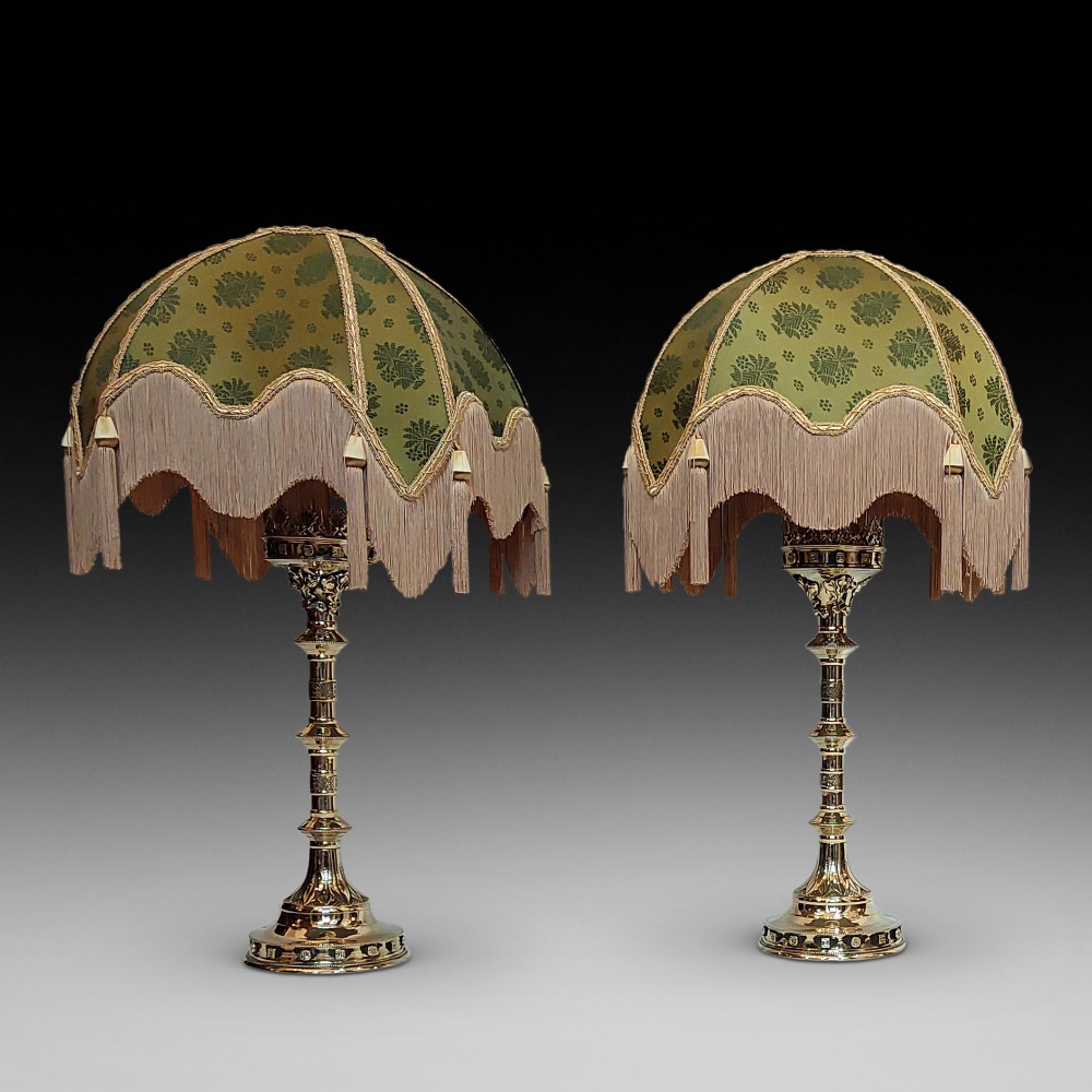 A pair of 19th-century Gothic Revival cast brass table lamps featuring knopped columns and dome-shaped green patterned fabric shades with long fringe and tassels.
