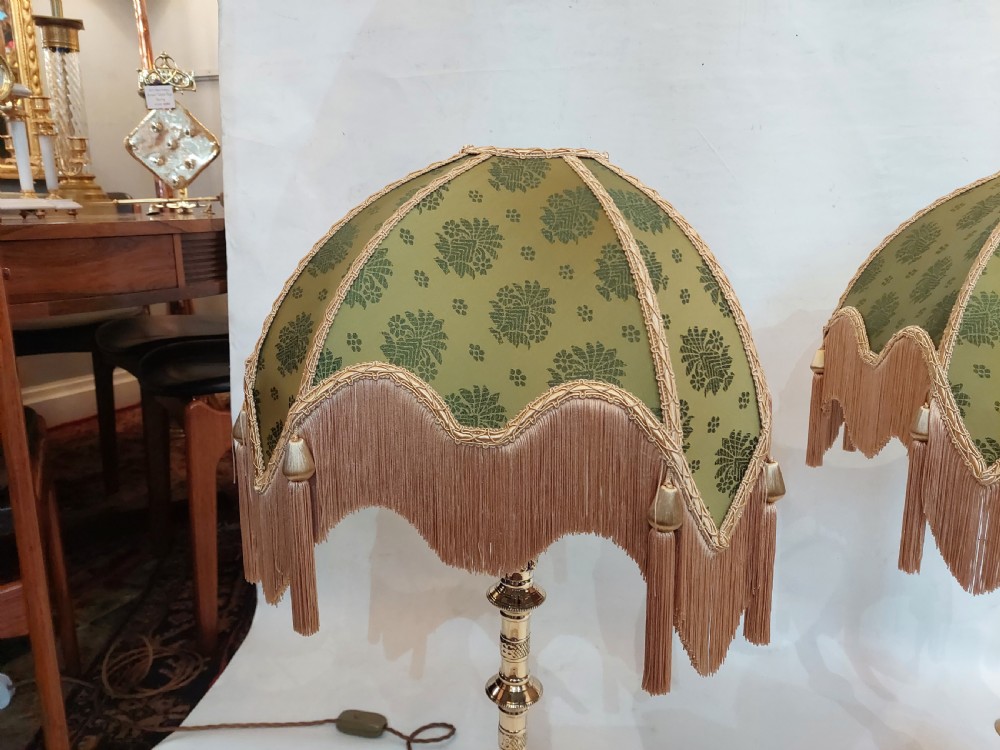 A pair of 19th-century Gothic Revival cast brass table lamps featuring knopped columns and dome-shaped green patterned fabric shades with long fringe and tassels. View VI