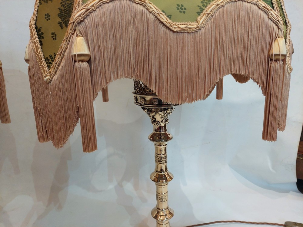 A pair of 19th-century Gothic Revival cast brass table lamps featuring knopped columns and dome-shaped green patterned fabric shades with long fringe and tassels. View VII
