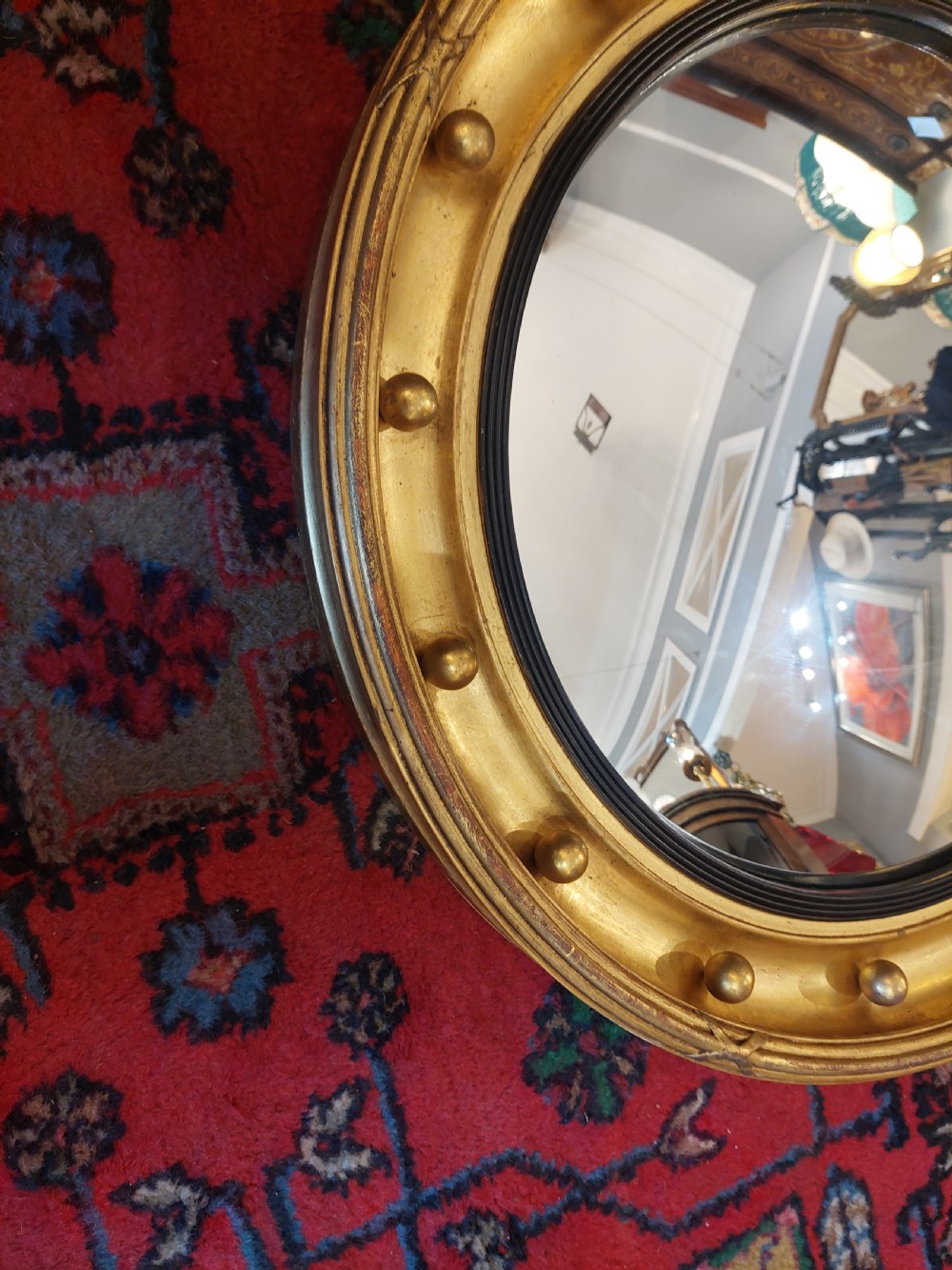 A 19th-century Regency style circular giltwood convex mirror decorated with spherules along the frame and an ebonised inner slip. View II