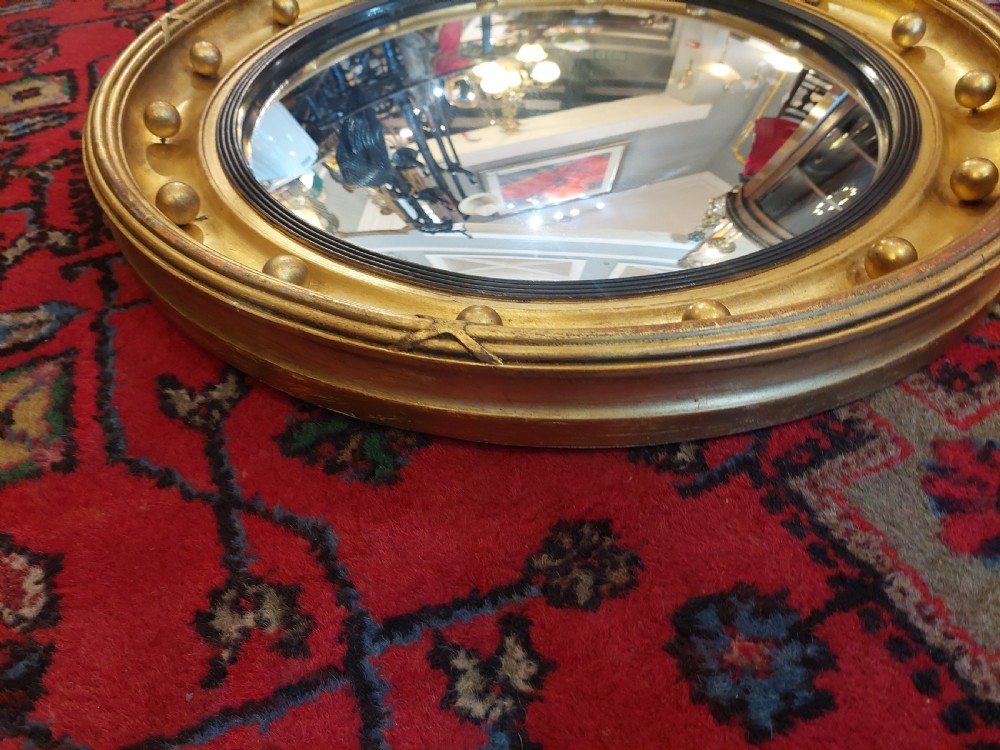 A 19th-century Regency style circular giltwood convex mirror decorated with spherules along the frame and an ebonised inner slip. View III