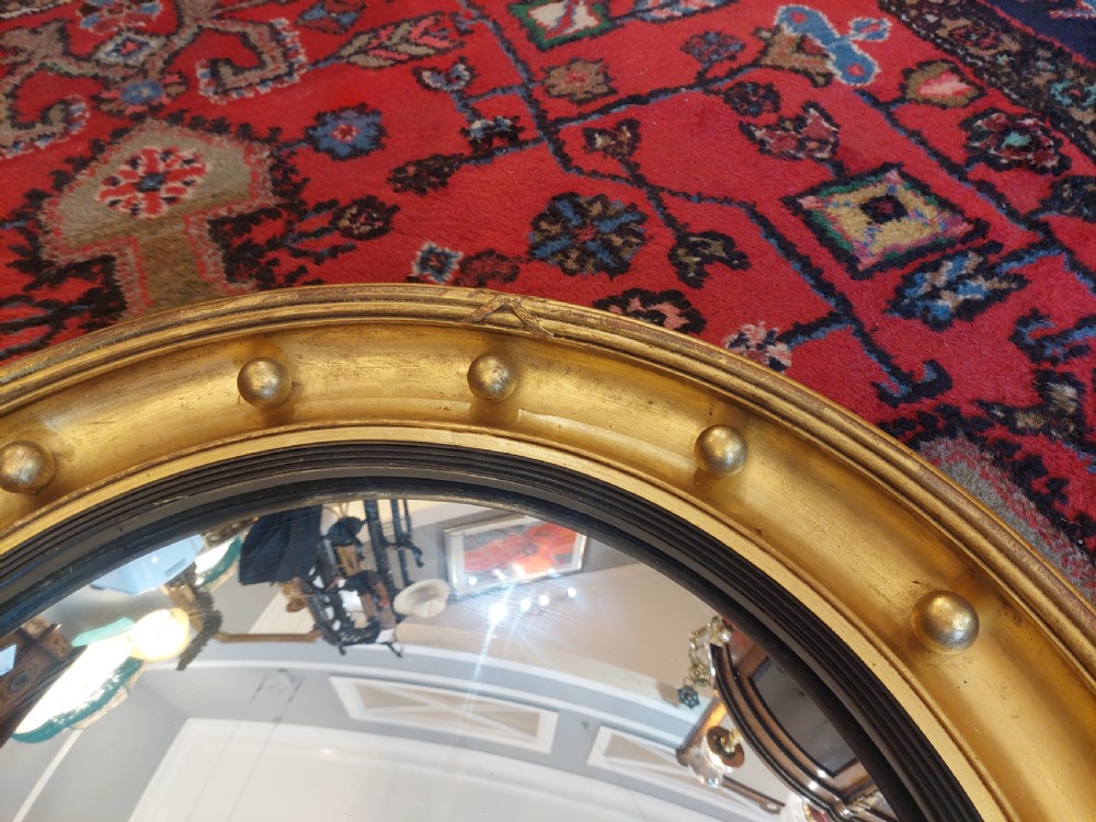 A 19th-century Regency style circular giltwood convex mirror decorated with spherules along the frame and an ebonised inner slip. View IV