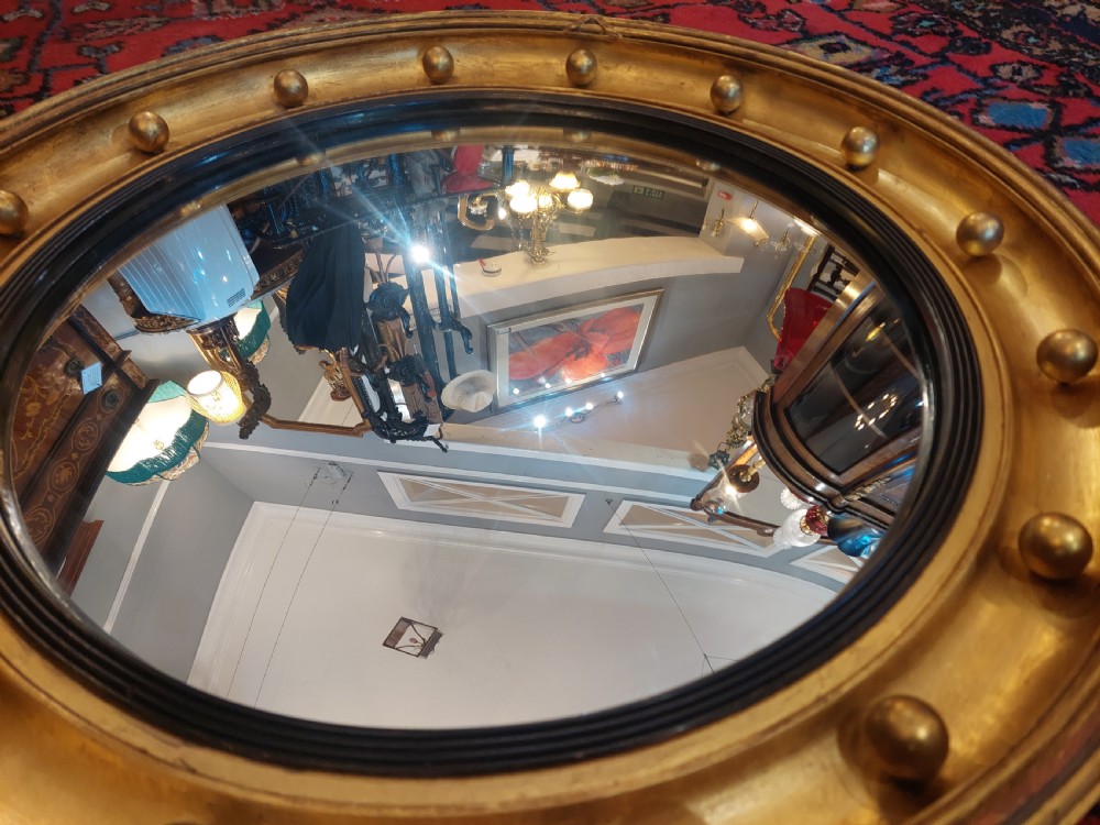 A 19th-century Regency style circular giltwood convex mirror decorated with spherules along the frame and an ebonised inner slip. View VI