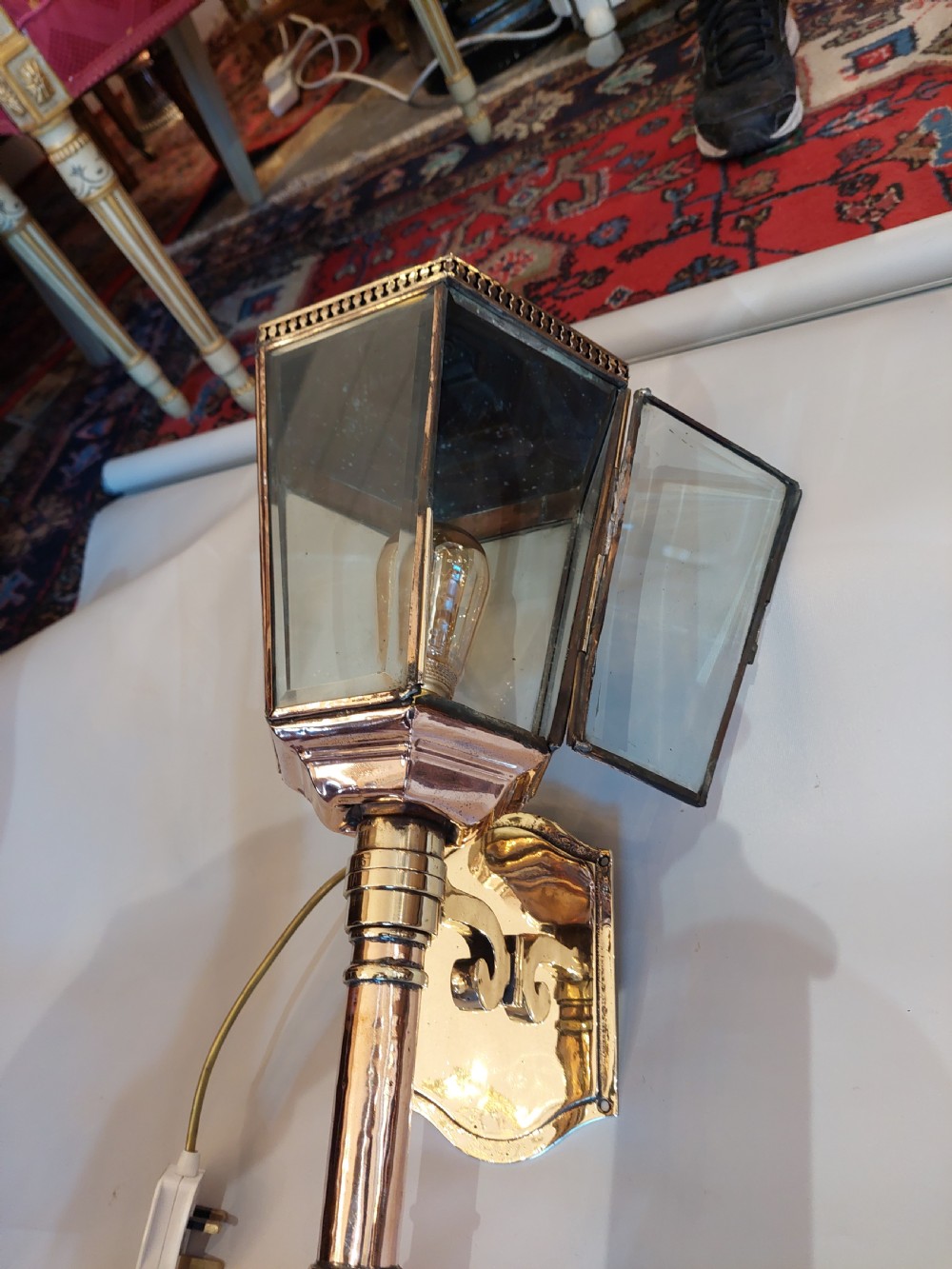 An Edwardian hexagonal wall-mounted porch lantern featuring polished brass and copper framing, clear glass panels, a pointed top finial, and a turned lower stem. View III