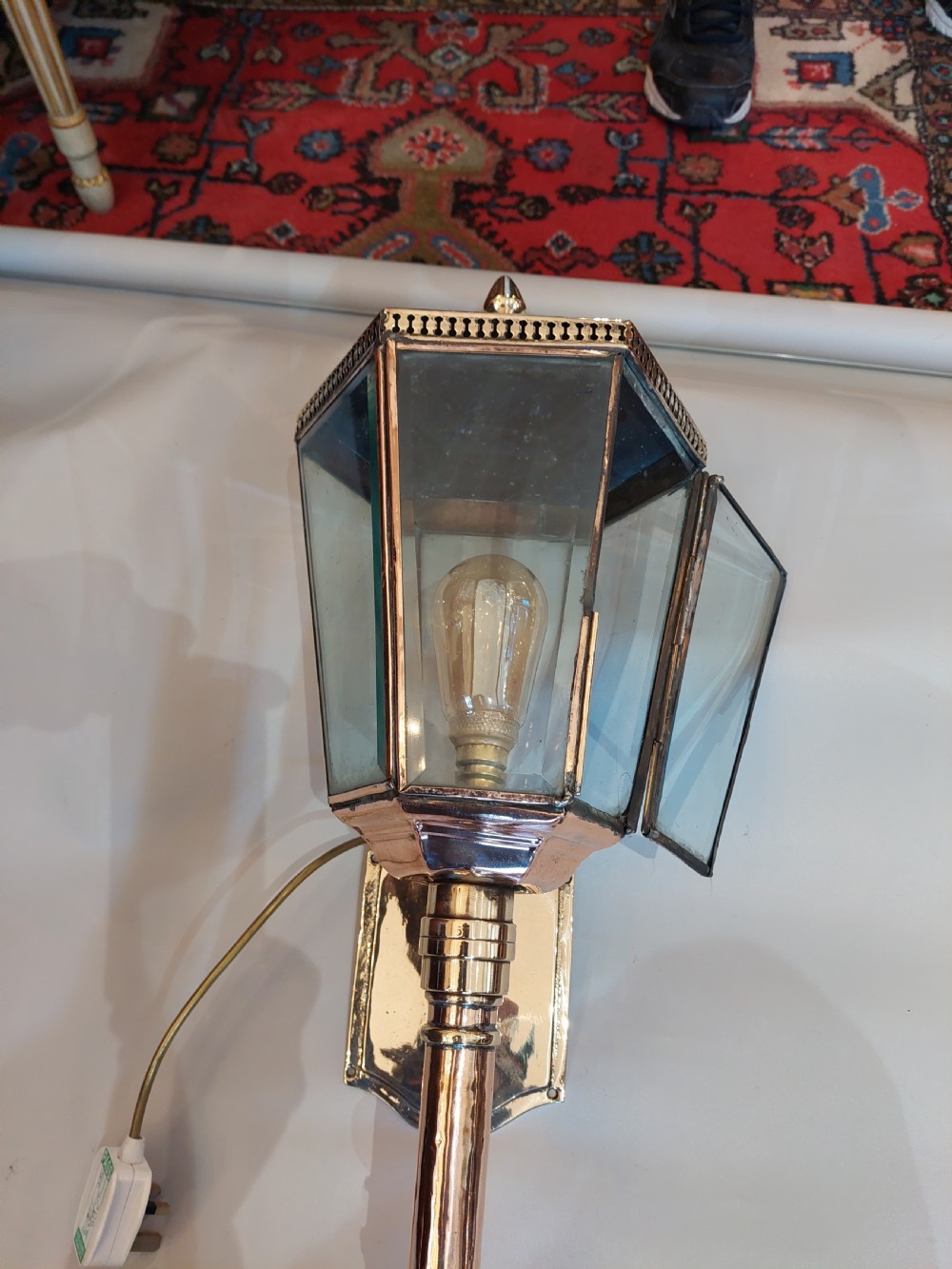An Edwardian hexagonal wall-mounted porch lantern featuring polished brass and copper framing, clear glass panels, a pointed top finial, and a turned lower stem. View IV