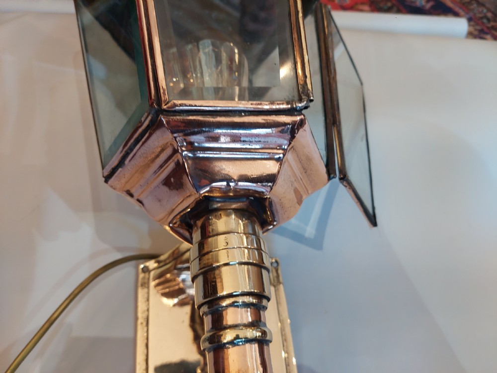 An Edwardian hexagonal wall-mounted porch lantern featuring polished brass and copper framing, clear glass panels, a pointed top finial, and a turned lower stem. View V