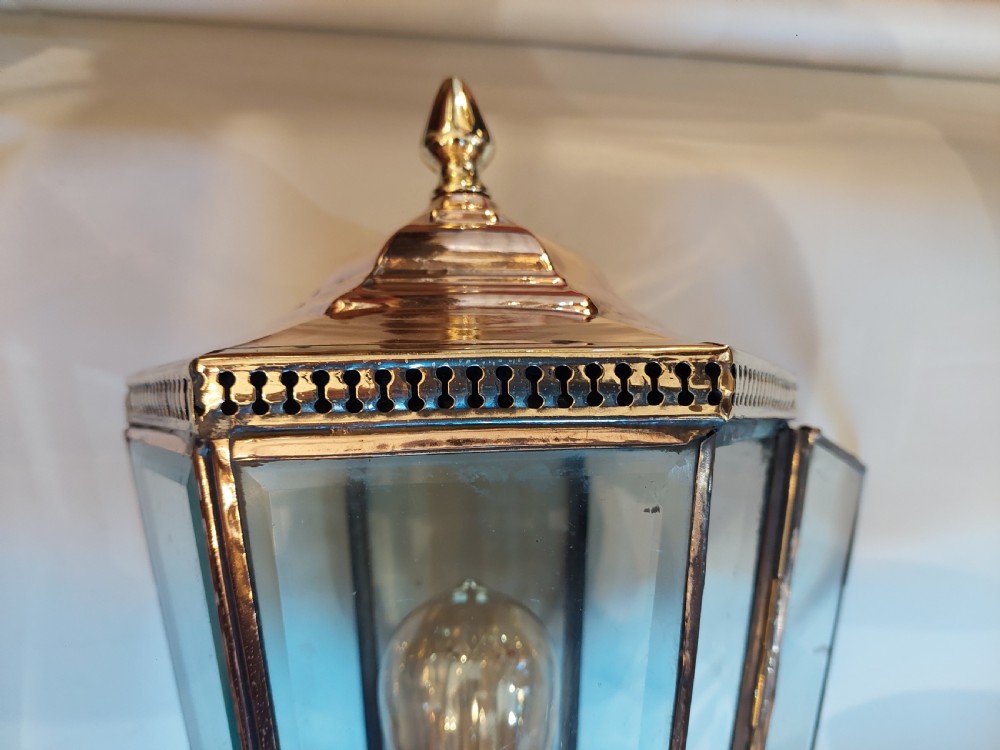 An Edwardian hexagonal wall-mounted porch lantern featuring polished brass and copper framing, clear glass panels, a pointed top finial, and a turned lower stem. View VI