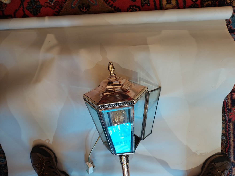 An Edwardian hexagonal wall-mounted porch lantern featuring polished brass and copper framing, clear glass panels, a pointed top finial, and a turned lower stem. View VIII