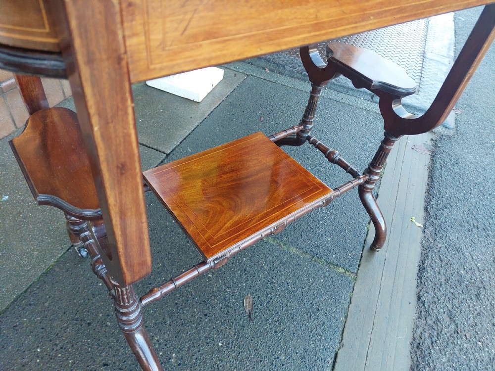 An Edwardian mahogany side table featuring decorative string inlay, a lower shelf, shaped side supports, and legs with brass castors. View IV