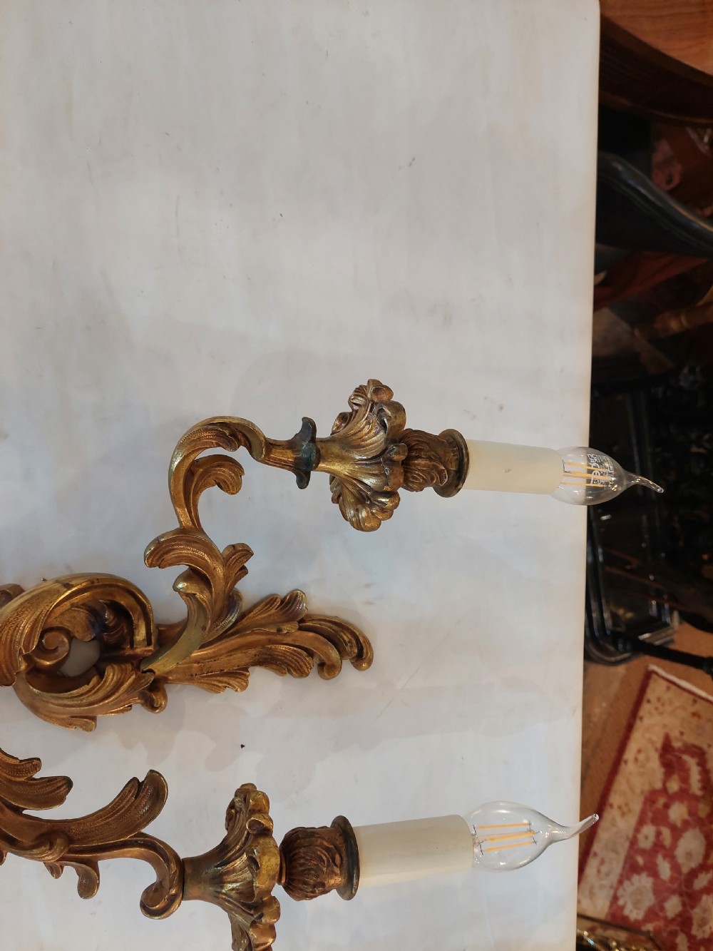 Set of four early twentieth-century cast brass two-arm wall lights featuring ornate Rococo scrolling foliage backplates and candle sockets. View IV