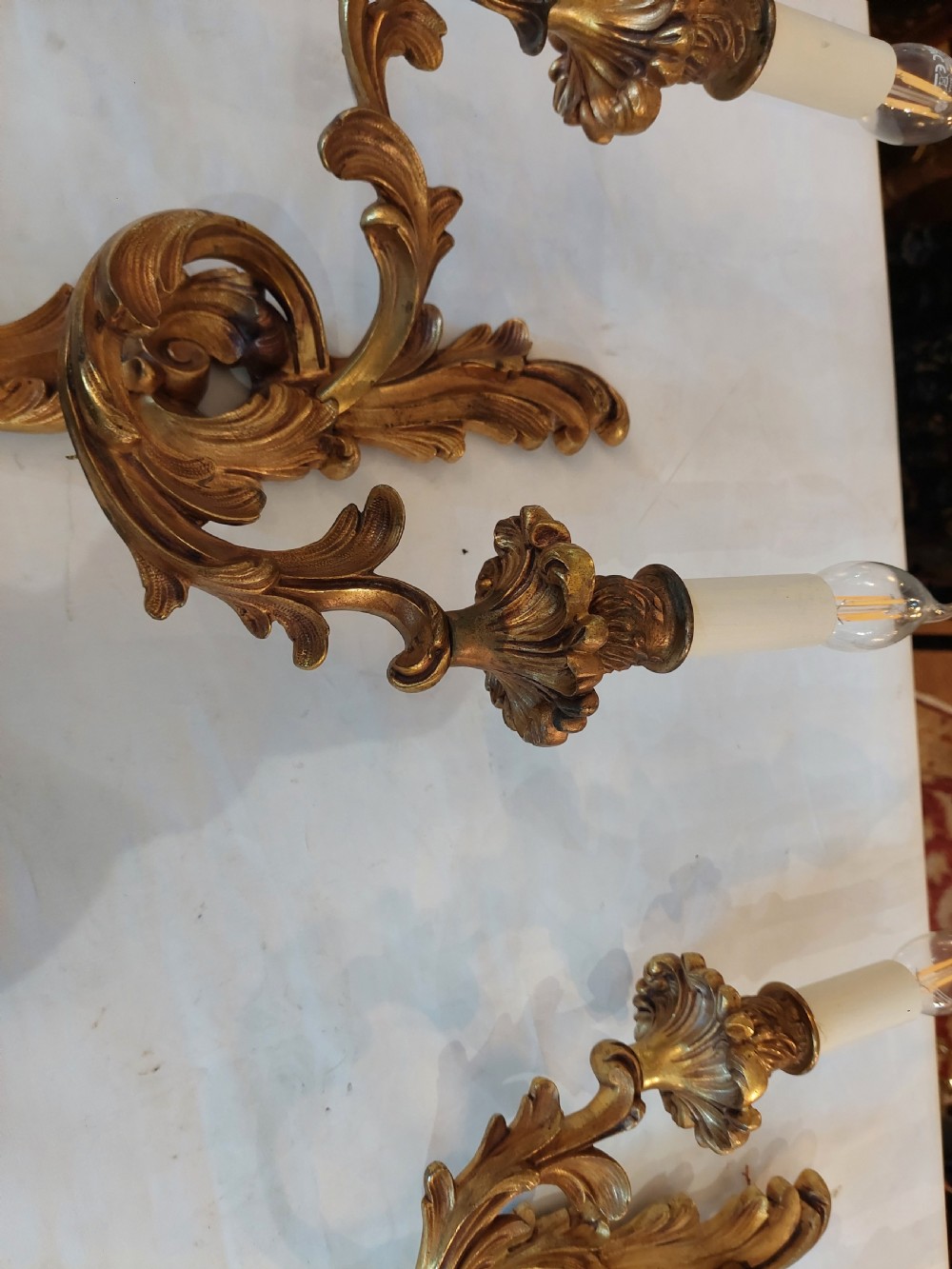 Set of four early twentieth-century cast brass two-arm wall lights featuring ornate Rococo scrolling foliage backplates and candle sockets. View VI