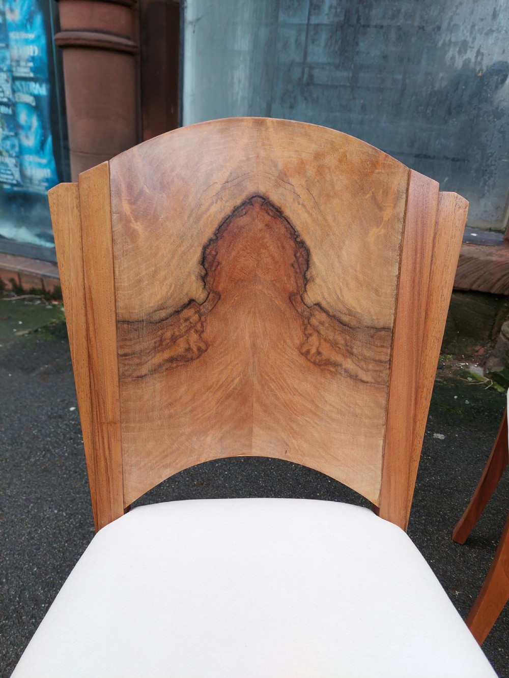 An Art Deco walnut dining suite comprising an oval pedestal table and six matching chairs with arched burr walnut backs and cream upholstered seats. View II
