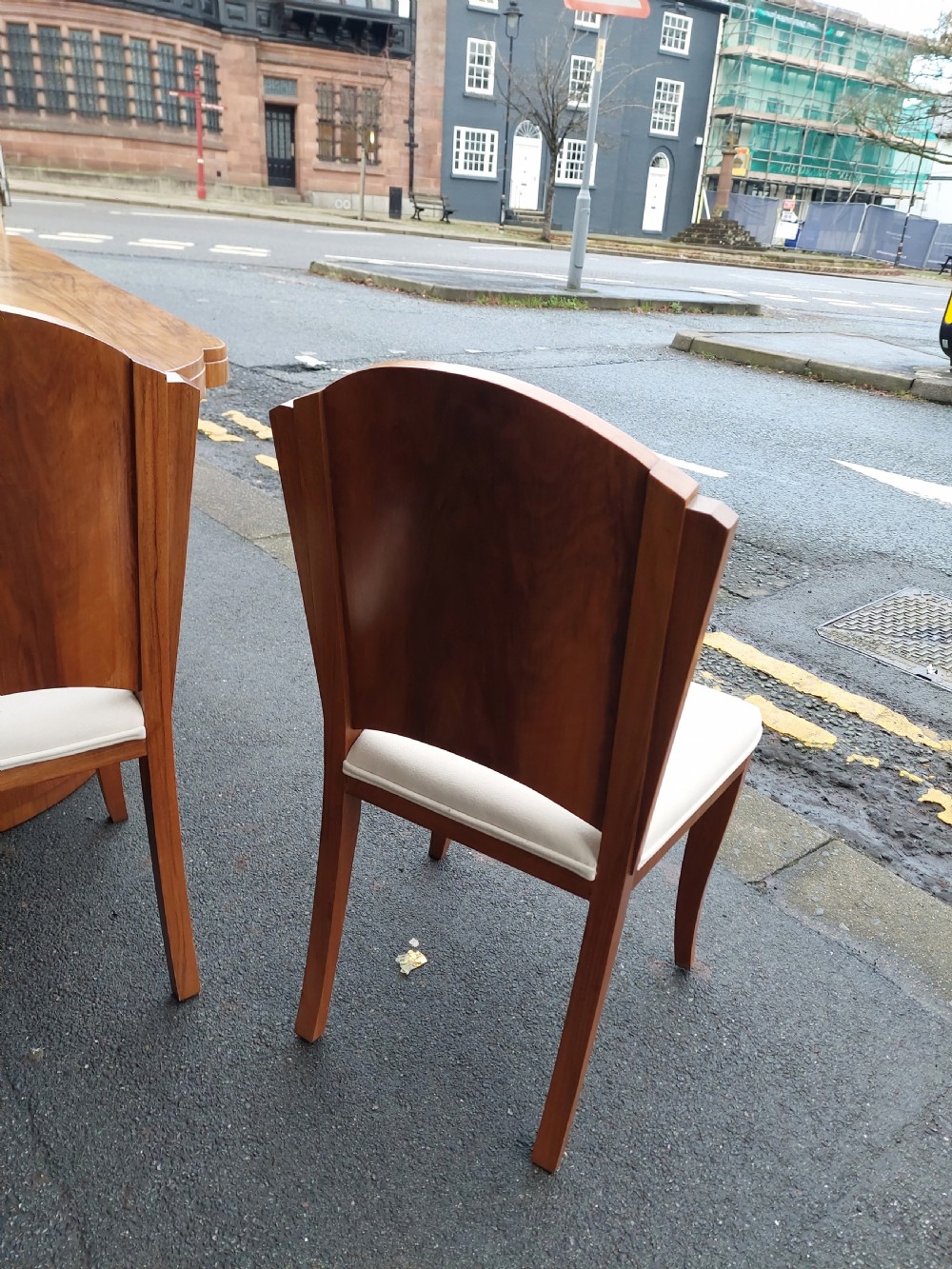 An Art Deco walnut dining suite comprising an oval pedestal table and six matching chairs with arched burr walnut backs and cream upholstered seats. View V