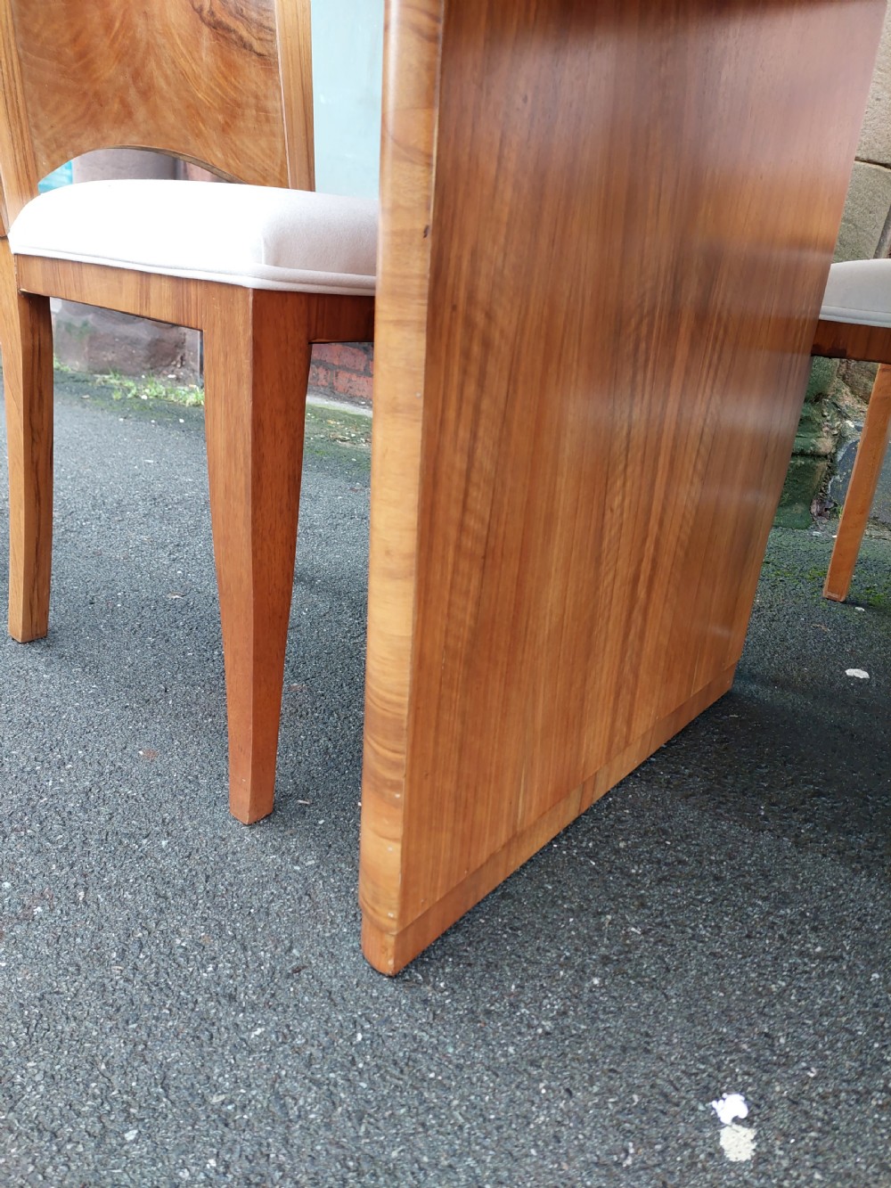 An Art Deco walnut dining suite comprising an oval pedestal table and six matching chairs with arched burr walnut backs and cream upholstered seats. View VII