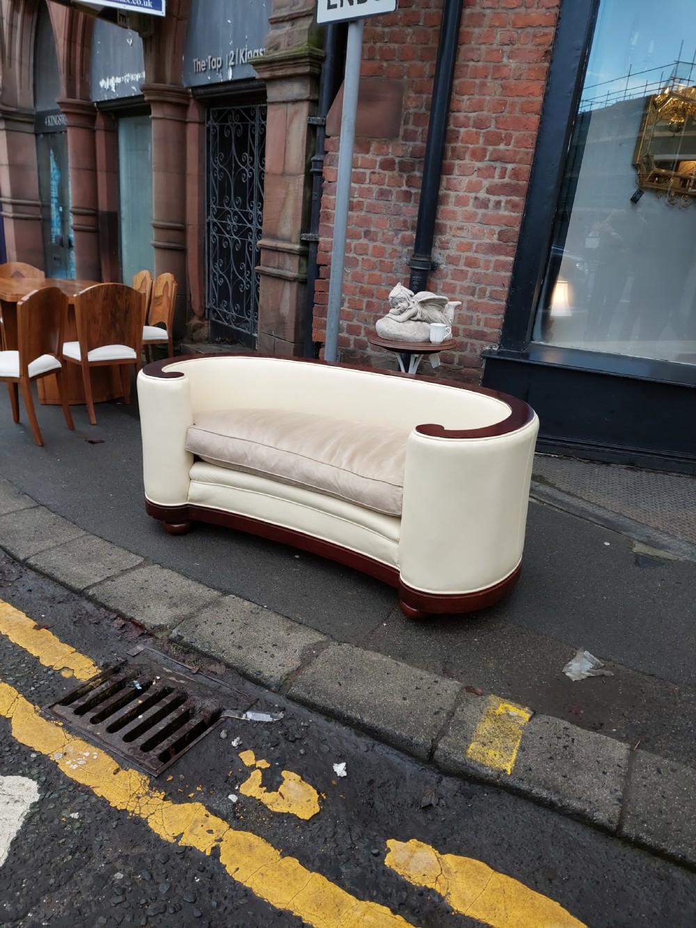 A curved Art Deco sofa featuring cream leather upholstery, a soft seat cushion, and polished palisander wood scroll trims on a low wooden base. View II