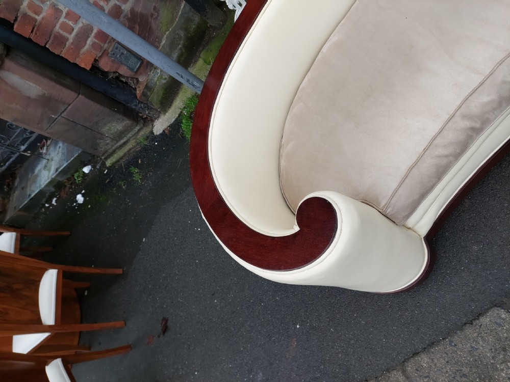 A curved Art Deco sofa featuring cream leather upholstery, a soft seat cushion, and polished palisander wood scroll trims on a low wooden base. View III