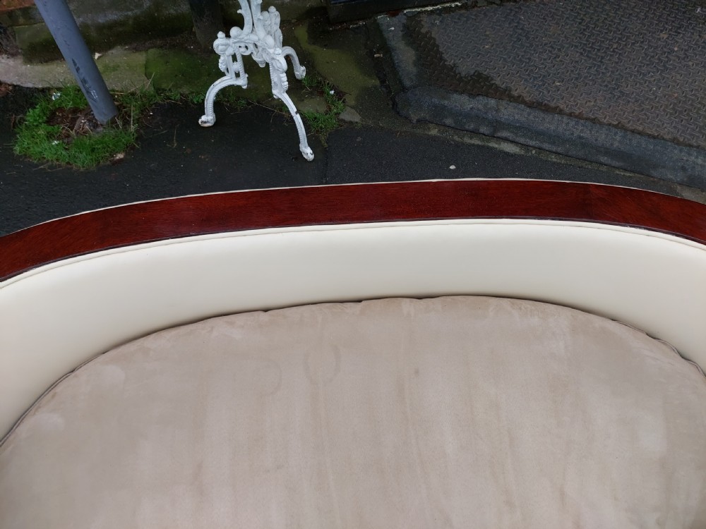A curved Art Deco sofa featuring cream leather upholstery, a soft seat cushion, and polished palisander wood scroll trims on a low wooden base. View IV