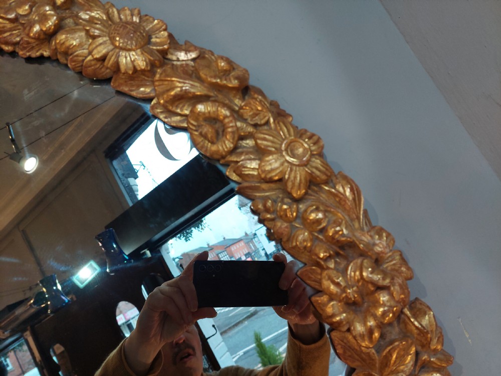 An oval Victorian wall mirror featuring a giltwood frame carved with floral motifs and a tied ribbon detail at the base. View VII