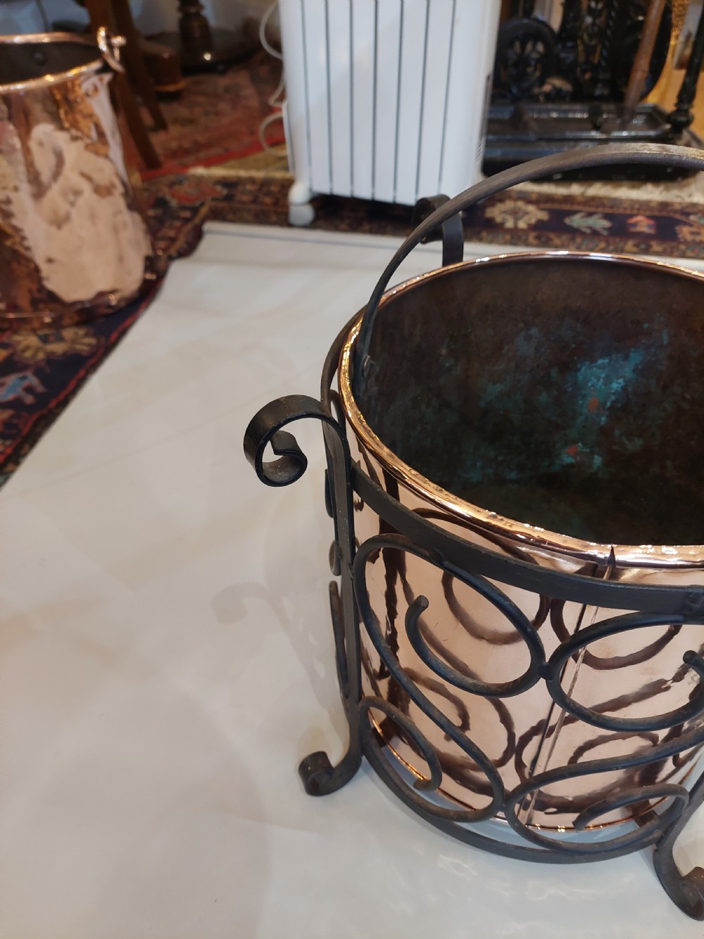 A cylindrical copper bucket set within a black wrought iron frame featuring scroll motifs and a curved carrying handle. View III