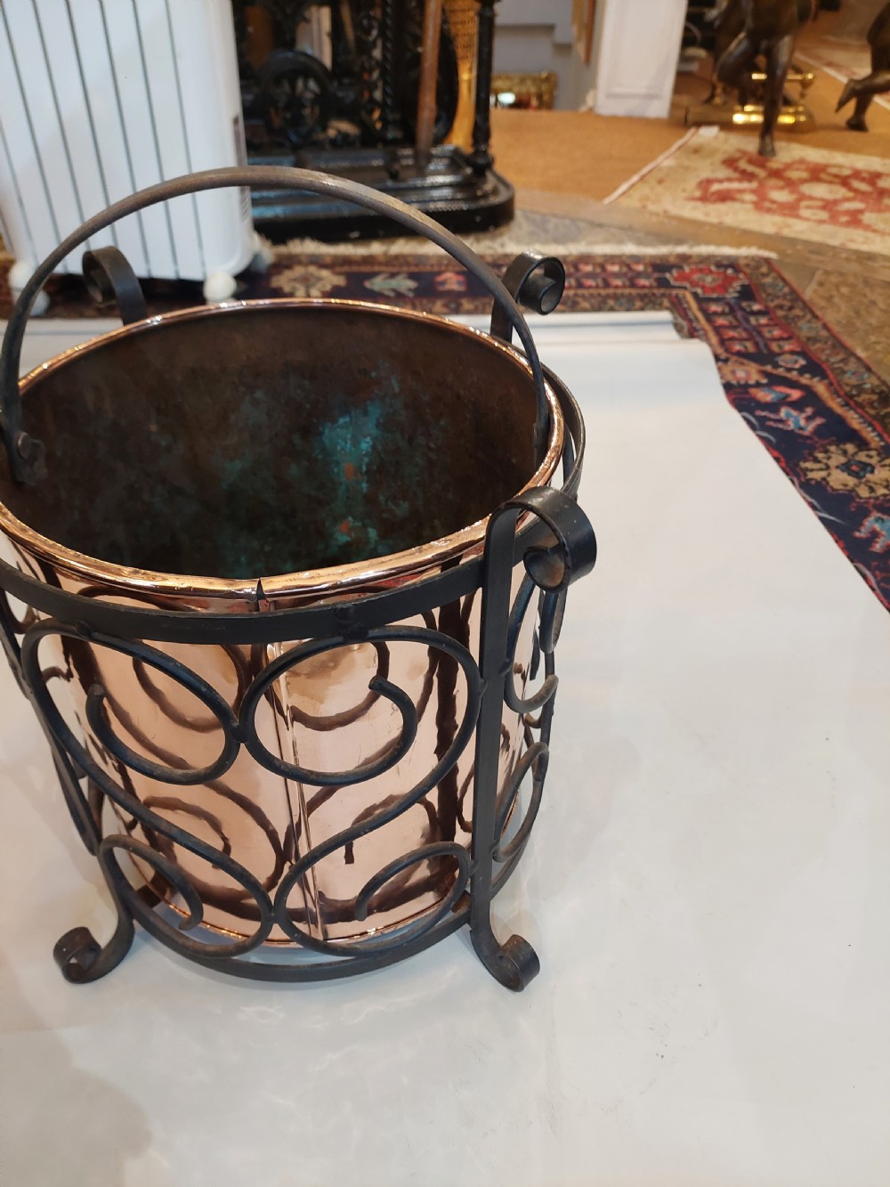 A cylindrical copper bucket set within a black wrought iron frame featuring scroll motifs and a curved carrying handle. View IV