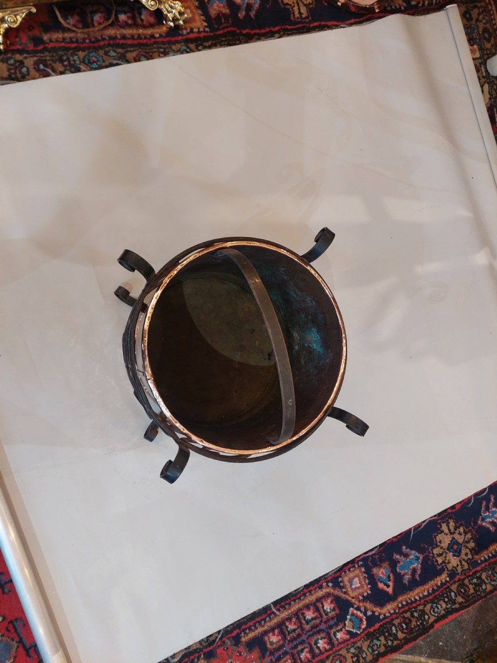 A cylindrical copper bucket set within a black wrought iron frame featuring scroll motifs and a curved carrying handle. View V