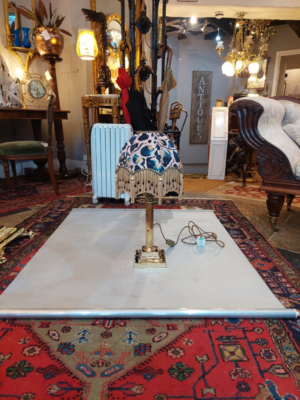 An early 20th-century brass Corinthian column table lamp with a stepped square base and a dome-shaped patterned silk shade featuring fringed tassels. View II