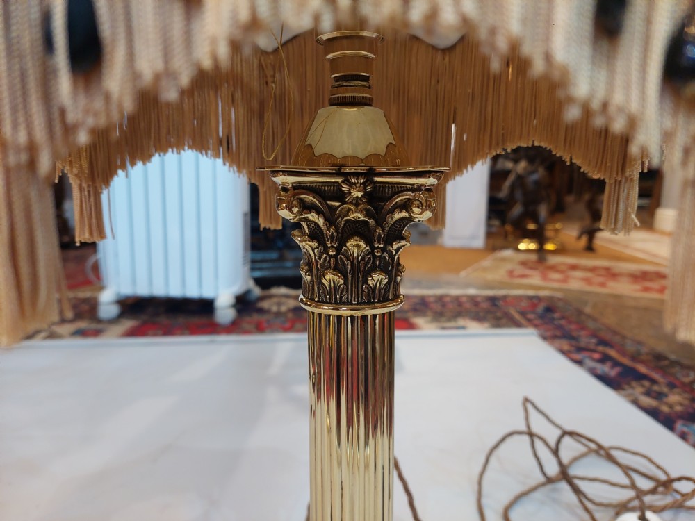 An early 20th-century brass Corinthian column table lamp with a stepped square base and a dome-shaped patterned silk shade featuring fringed tassels. View V