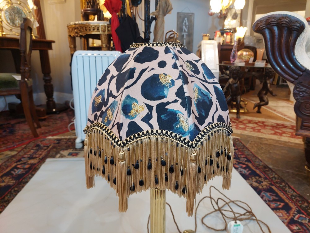 An early 20th-century brass Corinthian column table lamp with a stepped square base and a dome-shaped patterned silk shade featuring fringed tassels. View VI