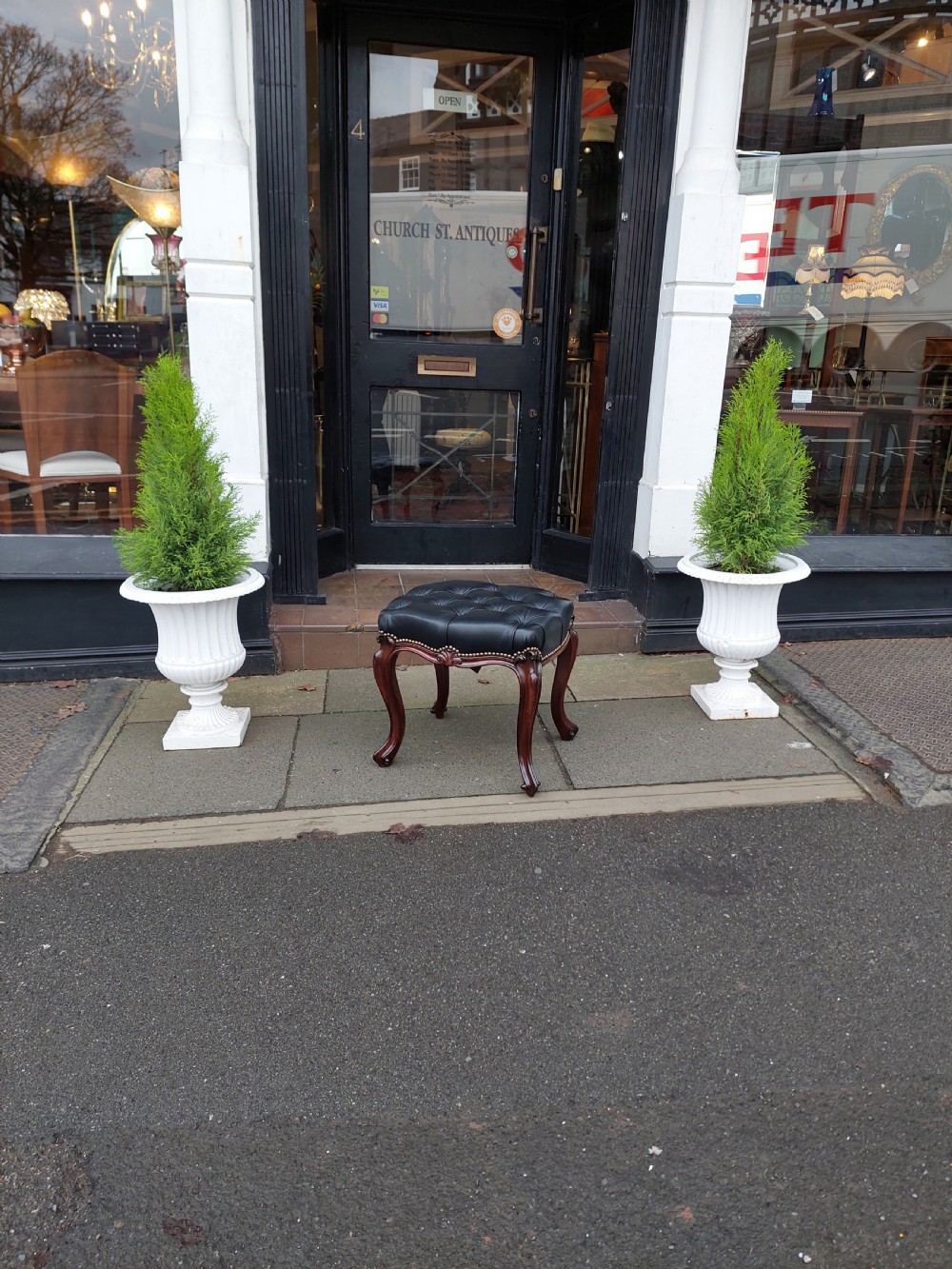 A Victorian mahogany stool featuring dark buttoned black leather upholstery with brass studding and four carved cabriole legs. View II