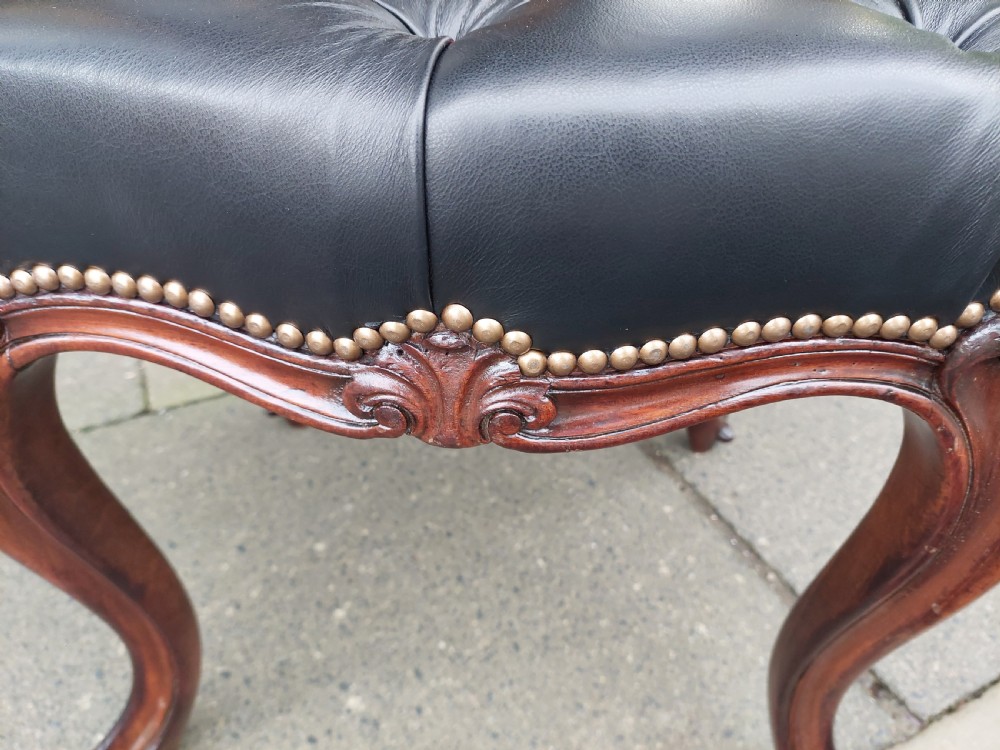A Victorian mahogany stool featuring dark buttoned black leather upholstery with brass studding and four carved cabriole legs. View III