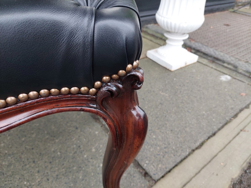 A Victorian mahogany stool featuring dark buttoned black leather upholstery with brass studding and four carved cabriole legs. View IV