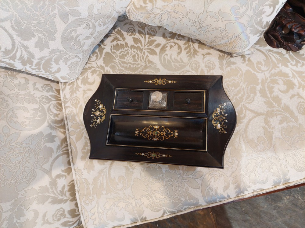 A mid-19th-century dark coromandel wood inkstand desk tidy featuring floral inlay, a pen trough, two lidded compartments, and a central glass inkwell. View II