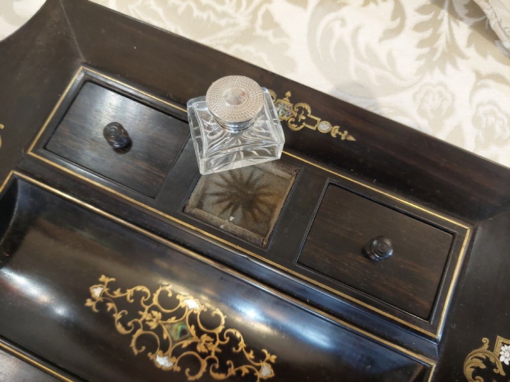 A mid-19th-century dark coromandel wood inkstand desk tidy featuring floral inlay, a pen trough, two lidded compartments, and a central glass inkwell. View IV