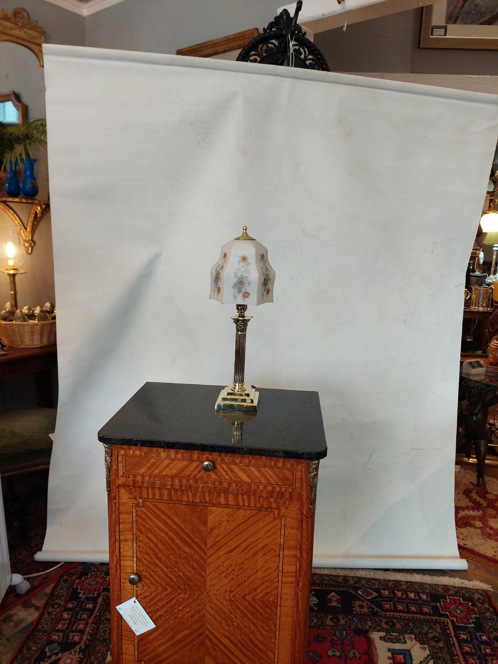 A polished brass table lamp designed as a fluted Corinthian column on a stepped square base, topped with a scalloped cream fabric shade decorated with embroidered floral motifs. View II