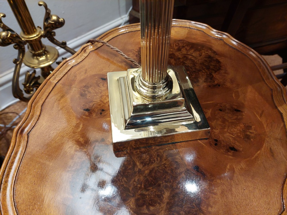 A polished brass table lamp designed as a fluted Corinthian column on a stepped square base, topped with a scalloped cream fabric shade decorated with embroidered floral motifs. View V