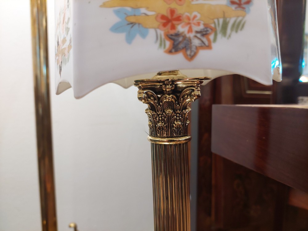 A polished brass table lamp designed as a fluted Corinthian column on a stepped square base, topped with a scalloped cream fabric shade decorated with embroidered floral motifs. View VI
