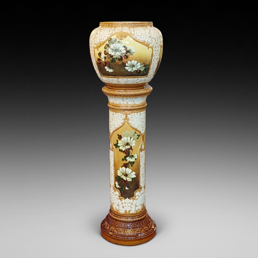 A Victorian Burmantofts majolica ceramic jardiniere and matching pedestal stand featuring painted floral panels and cream relief scrollwork on an ochre glaze.