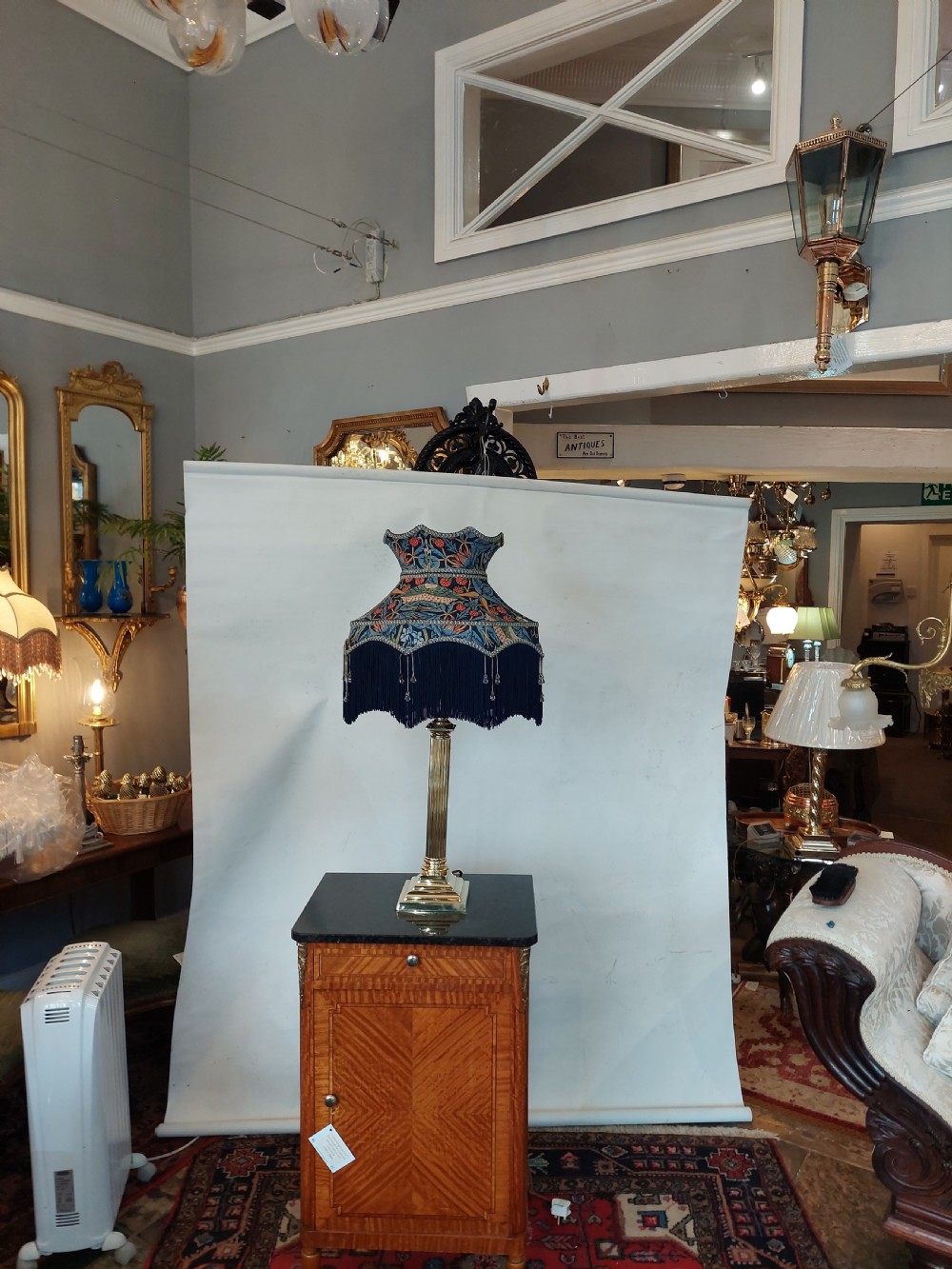 An early 20th-century brass table lamp featuring a reeded Doric column base and a patterned fabric lampshade with dark blue fringe and crystal drop beads. View II
