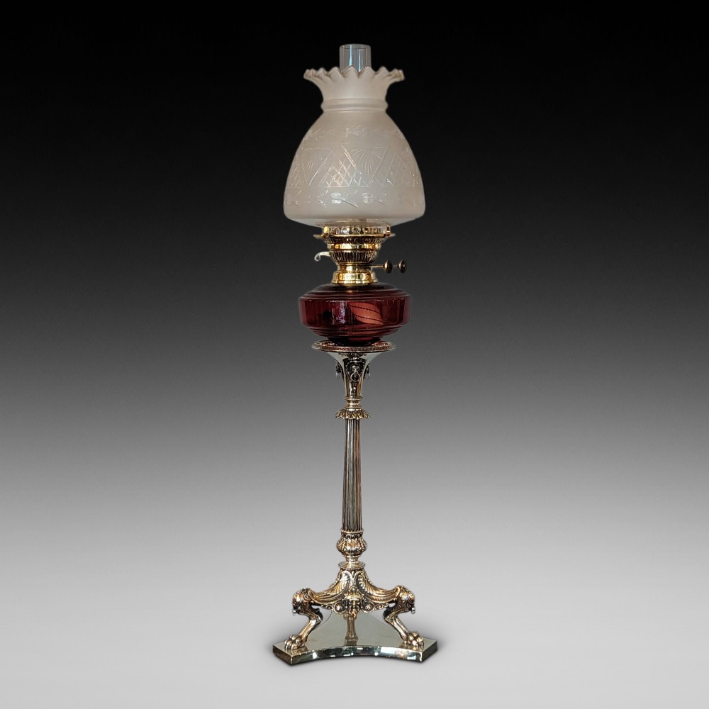 A late Victorian silver-plated oil lamp featuring a fluted column stem, a red cranberry glass reservoir, a brass burner, and a frosted etched glass shade.