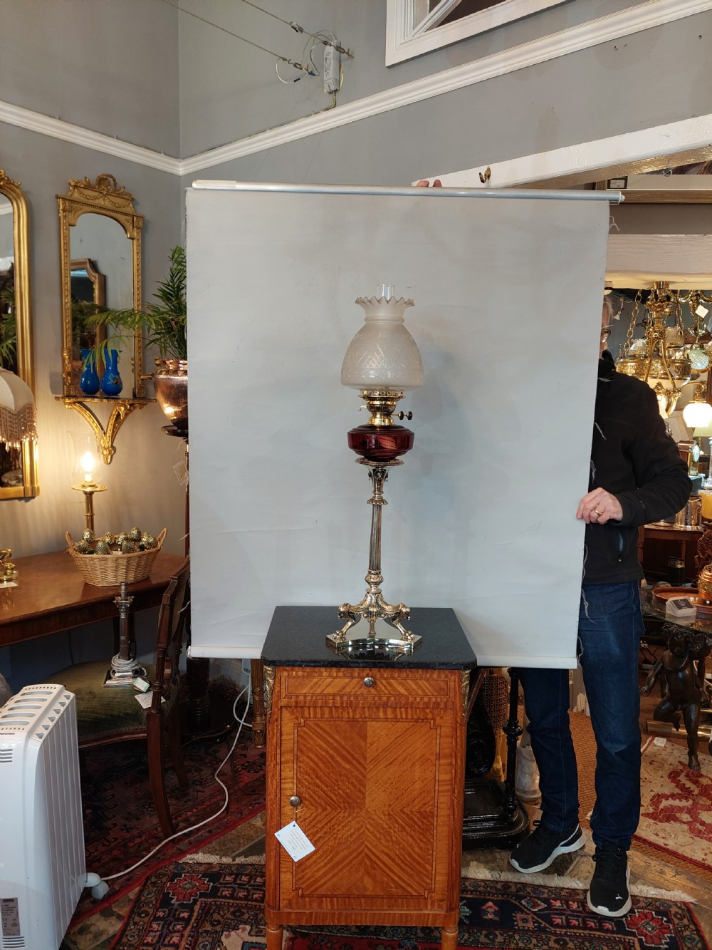 A late Victorian silver-plated oil lamp featuring a fluted column stem, a red cranberry glass reservoir, a brass burner, and a frosted etched glass shade. View II
