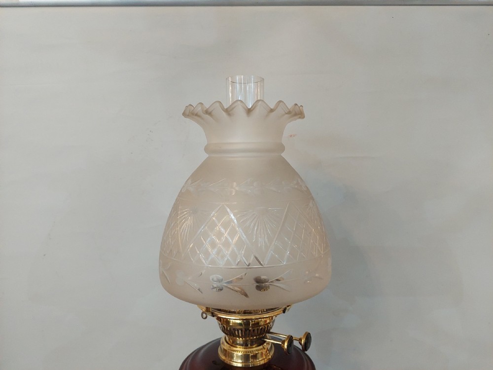 A late Victorian silver-plated oil lamp featuring a fluted column stem, a red cranberry glass reservoir, a brass burner, and a frosted etched glass shade. View V