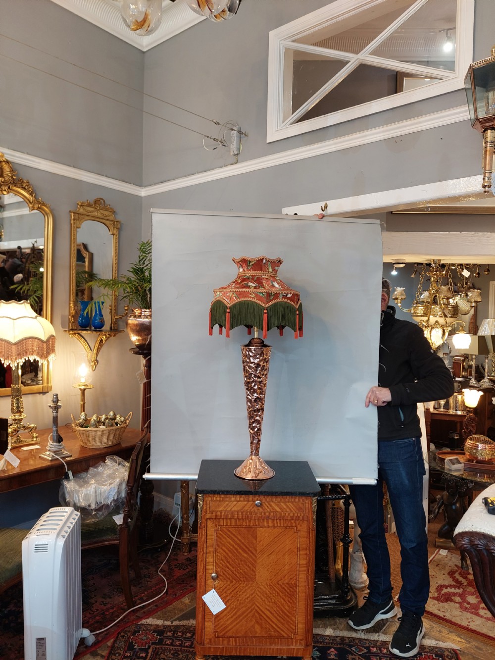An Arts and Crafts style table lamp featuring a tall, tapered beaten copper base topped with a decorative fringed fabric lampshade. View II