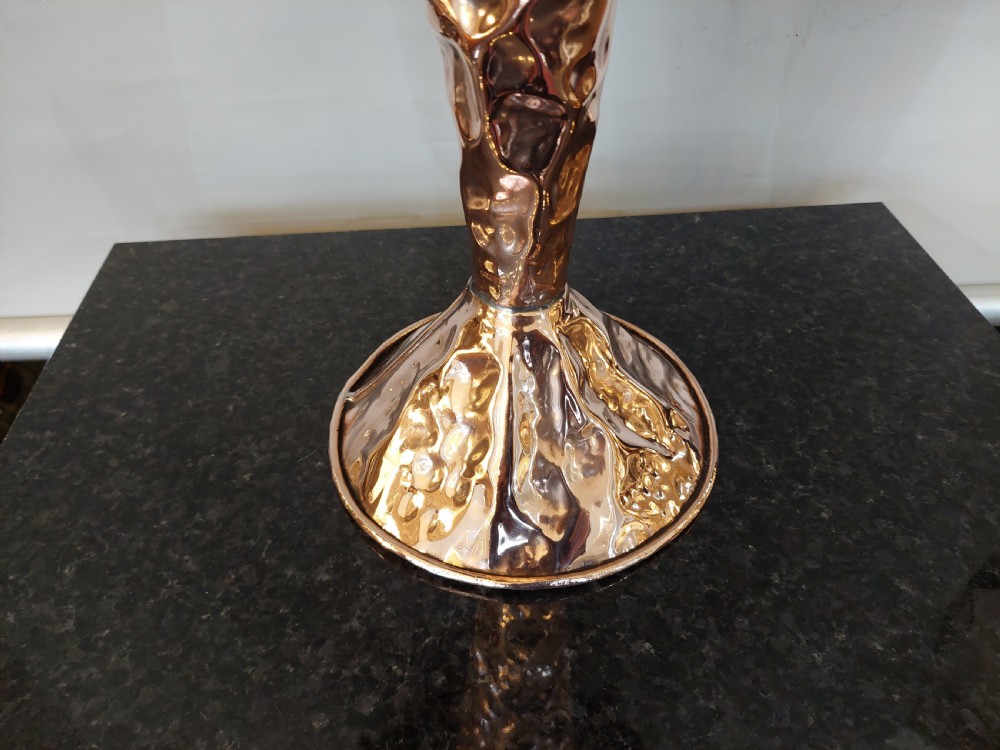 An Arts and Crafts style table lamp featuring a tall, tapered beaten copper base topped with a decorative fringed fabric lampshade. View IV