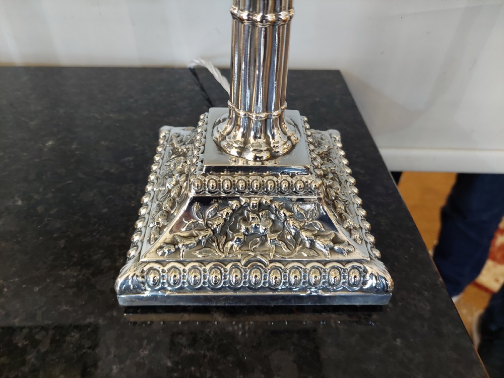 A pair of silver-plated table lamps designed as fluted classical columns with square relief-carved bases and cream square fabric lampshades. View II