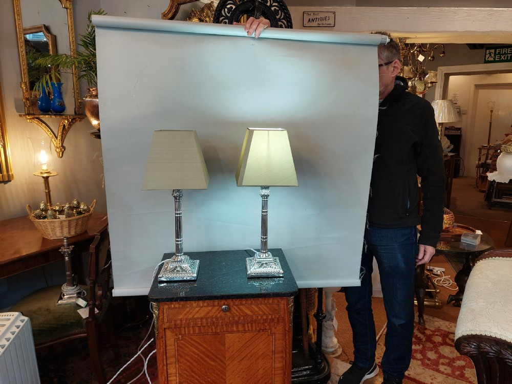 A pair of silver-plated table lamps designed as fluted classical columns with square relief-carved bases and cream square fabric lampshades. View VIII