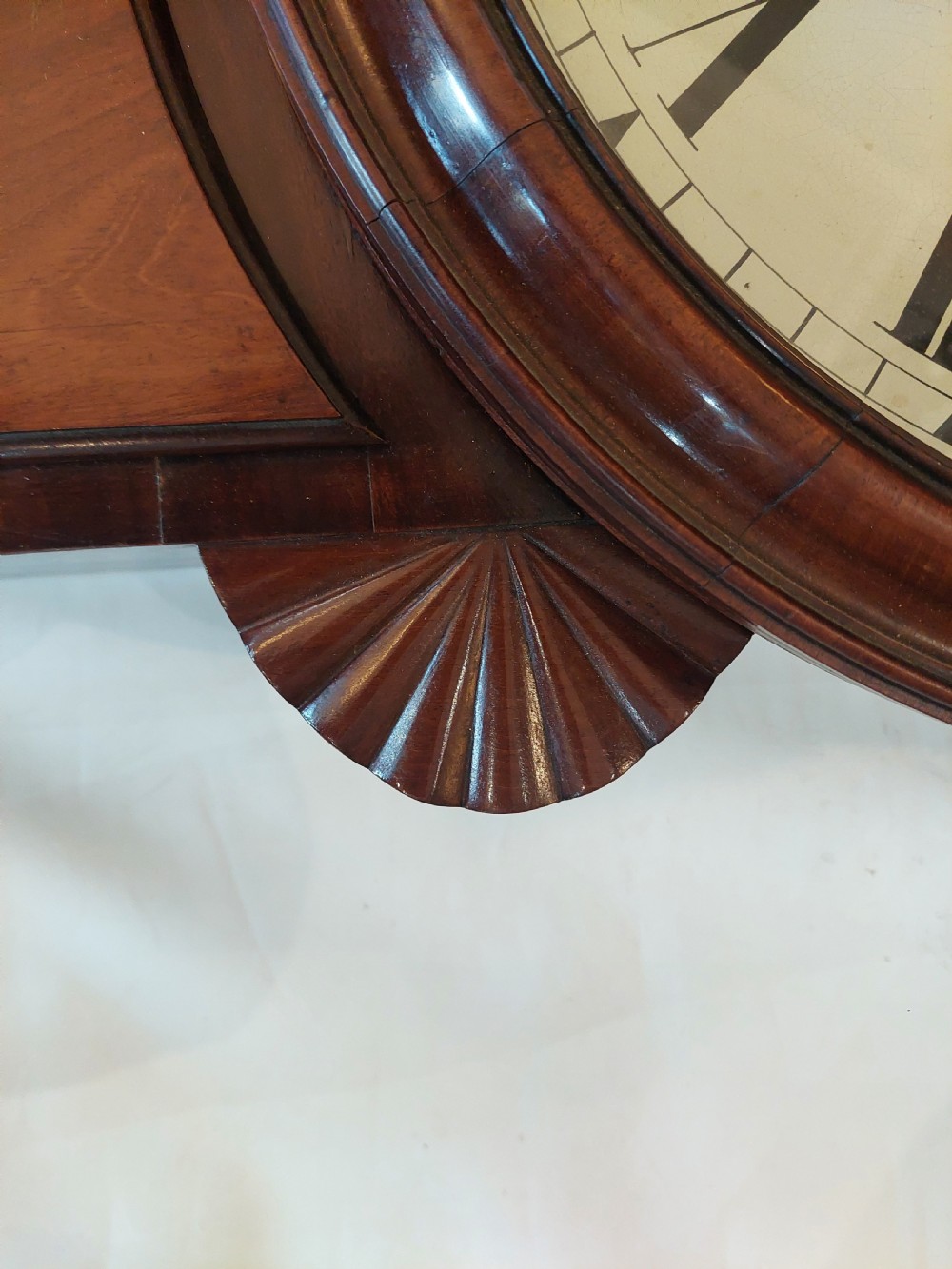 A George III mahogany drop dial wall clock featuring a white circular dial with Roman numerals above a flame mahogany trunk door. View VI
