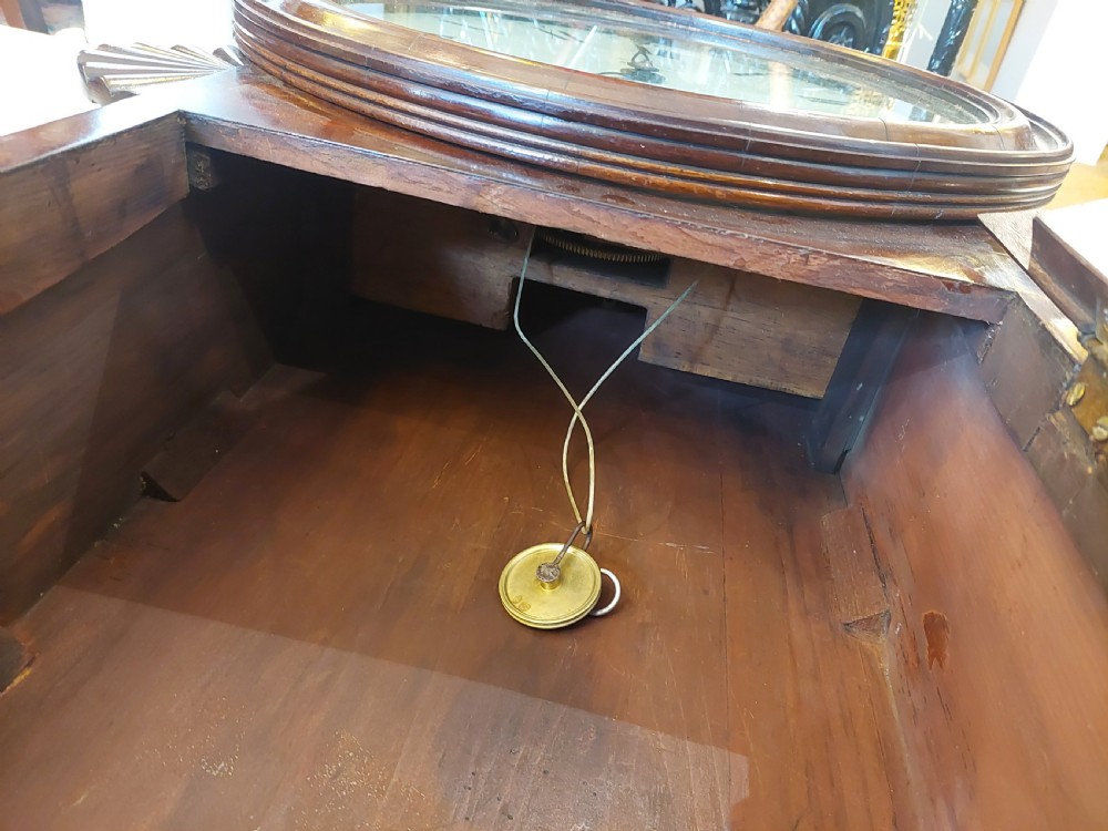A George III mahogany drop dial wall clock featuring a white circular dial with Roman numerals above a flame mahogany trunk door. View VIII